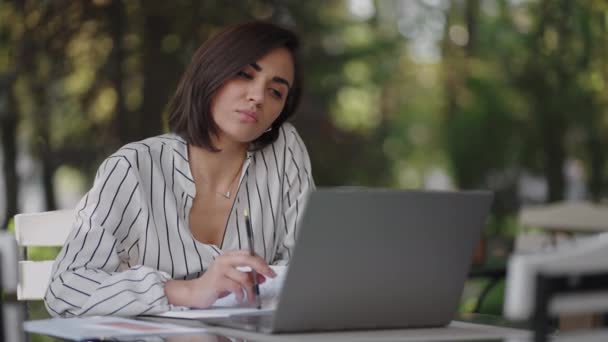 Pensive žena Bruneta arabské hispánské etnické skupiny sedí u stolu v letní kavárně s notebookem. Vážná podnikatelka přemýšlející o řešení problémů a strategie rozvoje podnikání — Stock video