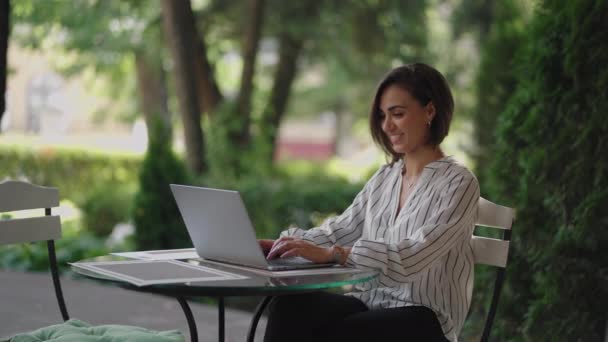 Mulher de negócios Morena árabe Grupo étnico hispânico está digitando em um laptop enquanto está sentado em uma mesa em um café de verão fazendo trabalho remoto. Mulher freelancer. Pequenas empresas — Vídeo de Stock