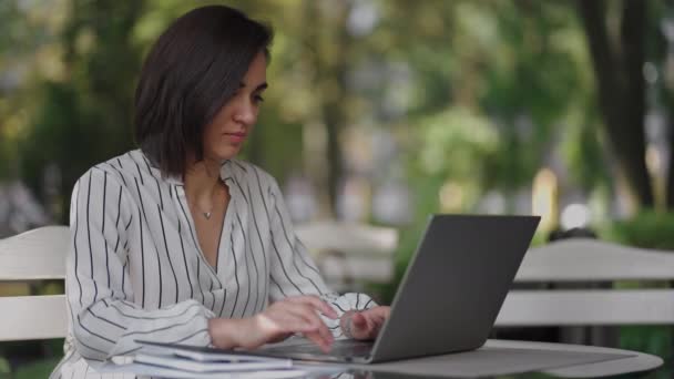 Donna d'affari Bruna Arabo Gruppo etnico ispanico sta digitando su un computer portatile mentre si siede a un tavolo in un caffè estivo facendo lavoro a distanza. Donna freelance. Piccole imprese — Video Stock