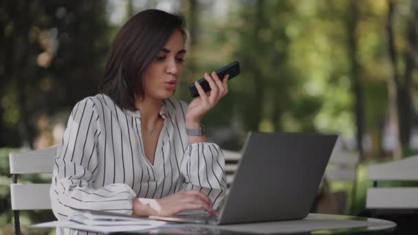 Mujer de negocios confiada grabando mensaje de audio en el teléfono inteligente en la calle. Mujer sentada en un café de verano utiliza el reconocimiento de voz smartphone, enviar mensaje de voz. altavoz o dejar el concepto de mensaje de voz — Vídeo de stock