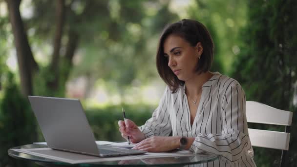 Mujer pensativa Morena árabe grupo étnico hispano se sienta en una mesa en un café de verano con un ordenador portátil. Mujer de negocios seria que reflexiona sobre la solución de problemas y la estrategia de desarrollo empresarial — Vídeos de Stock