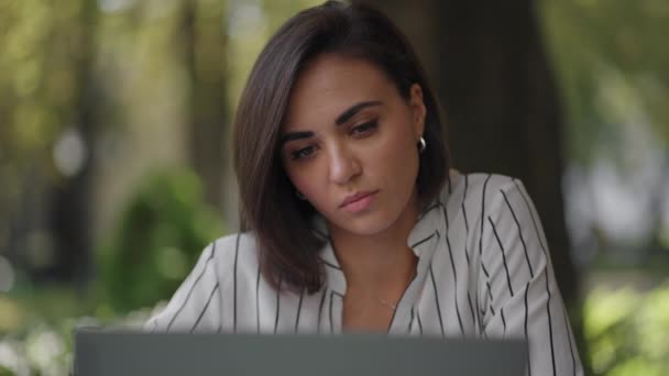 Talented Serious Woman Brunette Arab Hispanic ethnic group sits at a table in a summer cafe with a laptop. Considers solving problems. Puzzled business woman. portrait of a beautiful business woman — Stock Video