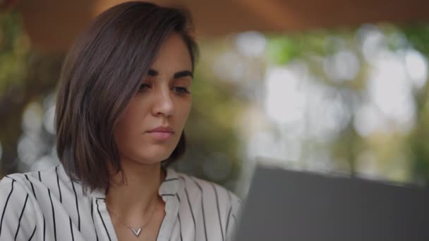 Geschäftsfrau Brünette arabisch-hispanische ethnische Gruppe tippt auf einem Laptop, während sie an einem Tisch in einem Sommercafé sitzt und Remote-Arbeit verrichtet. Freiberuflerin. Kleinunternehmen — Stockvideo