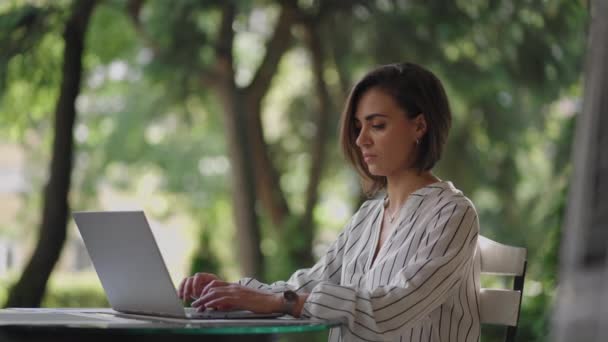 Бізнес-жінка Брунетт арабічна іспанська етнічна група друкує на ноутбуці, сидячи за столом у літньому кафе, виконуючи дистанційну роботу. Жінка-фрилансер. Маленький бізнес — стокове відео