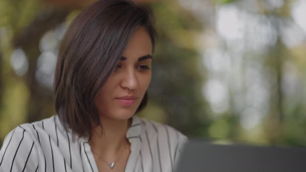 Retrato mulher séria Brunette árabe grupo étnico hispânico senta-se a uma mesa em um café de verão com um laptop. tipos no teclado e sofre treinamento on-line, compra e lida com um banco de Internet — Vídeo de Stock