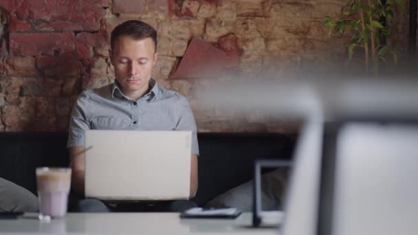 一个穿着衬衫的年轻人坐在桌旁，手里拿着笔记本电脑，键盘上打字。学生可以远程学习。商人经营他的生意遥不可及 — 图库视频影像