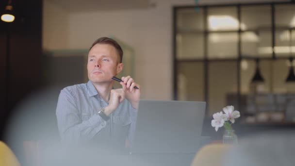 Närbild porträtt av ponder ung man i ämbetet. Designern planerar sitt arbete och håller en penna i handen. Skytte är slow motion underifrån. Tankeväckande seriös man sitta med laptop tänkande lösning — Stockvideo