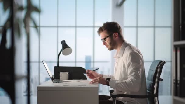 Retrato del hombre de negocios exitoso y reflexivo que trabaja en la computadora portátil en su oficina de la gran ciudad. Digital Entrepreneur hace análisis de datos para la estrategia de comercio electrónico. — Vídeo de stock