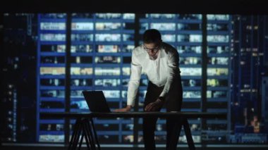 Gözlüklü sakallı bir Arap ve gece kulübünün arka planında duran bir gömlek ofis masasında duruyor ve beyin fırtınası yapıyor. Fazla mesai, gece işi, iş bulma.