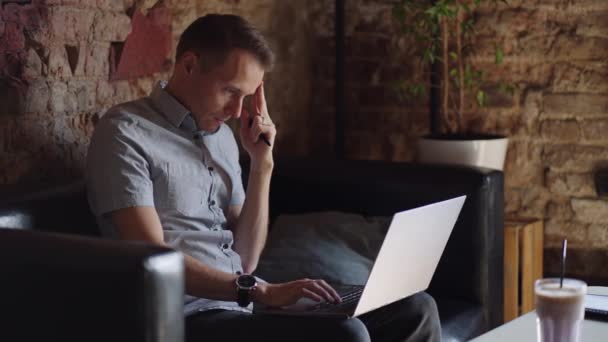 Close-up portrait of ponder young man in office. Designer plans his work and holding a pencil in his hand. Shooting is slow motion from below. Thoughtful serious man sit with laptop thinking solution — Stock Video