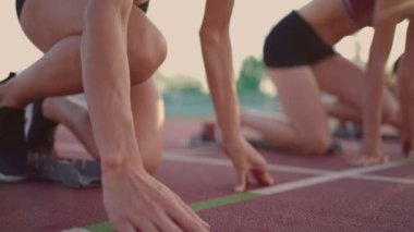 Tepedeki yarışmalarda, bir kadın ellerini yakın planda başlangıç çizgisine koyar. Yarış başladı. Stadyumdaki kadına yapılan yavaş çekim hazırlığı..