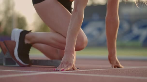 Női atléta futópályán kezdte a sprintelést. A futó elindul a futópálya rajtkockáiról. A fiatal női sportoló elkezd futni a háztömb elől. Lassú mozgás., — Stock videók