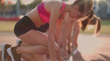 Başlangıç çizgisindeki stadyumda üç genç kadın ağır çekimde yarışa başlıyor.