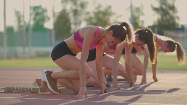 Tři mladé ženy na stadionu na startovní čáře v blocích začínají v závodě ve zpomaleném filmu — Stock video