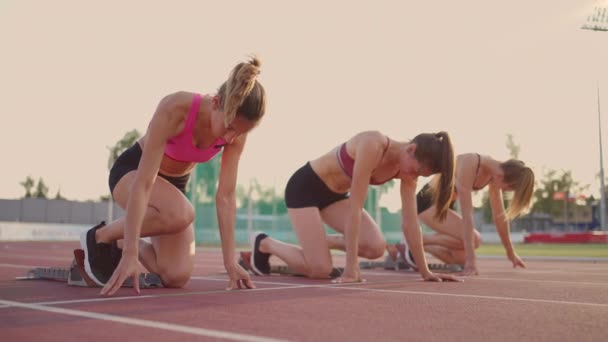 Tři mladé ženy na stadionu na startovní čáře v blocích začínají v závodě ve zpomaleném filmu — Stock video