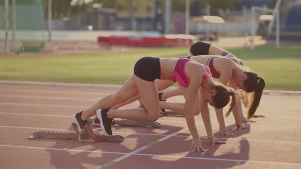 Tre unga kvinnor i stadion på startlinjen i block börjar i loppet i slow motion — Stockvideo