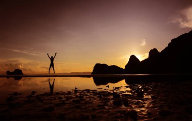 Erkekler sabahın köründe kumsalda zıplarken eğleniyorlar. Su yüzeyindeki yansımalar ve dağ arkası..
