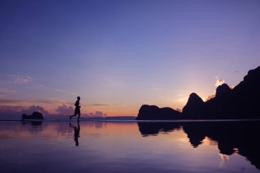 Sahilde gün doğumunda koşan adam, su, deniz ve dağ üzerinde yansıma, arka plan.