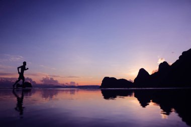 Sahilde gün doğumunda koşan adam, su, deniz ve dağ üzerinde yansıma, arka plan.