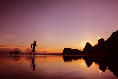 Sahilde gün doğumunda koşan adam, su, deniz ve dağ üzerinde yansıma, arka plan.