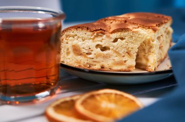 Bir bardak sıcak çay, elmalı turta ve mavi arka planda portakal dilimleri ve beyaz masa. Lezzetli kahvaltı ya da öğle yemeği konsepti