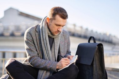 Beyaz sakallı, atkılı, gri ceketli, açık havada notlar alan bir adam. Güneşli bir bahar ya da sonbahar gününde erkek gibi düşünmek ve çalışmak. Çalışma ve öğrenim kavramı