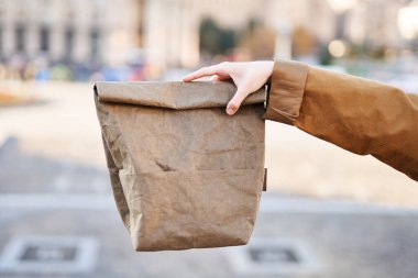 Şehrin arka planında sıfır atık kağıt torba taşıyan turuncu siperleri teslim edin. Ekolojik beslenme çantası ya da öğle yemeği konsepti