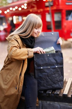 Çekici, genç, gülümseyen yeniyetme kadın akşam üstü sırt çantasıyla kırmızı çift katlı arka planda oturuyor. Alışveriş konsepti