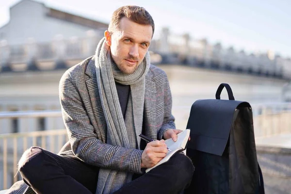 Eşarplı ve ceketli çekici bir iş adamı kameraya bakıyor, not defteriyle oturuyor. Çalışma ve öğrenim kavramı.