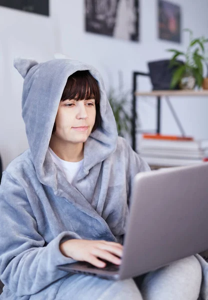 가운을 브루넷의 매력적 소녀가 침대에 거리를 컴퓨터로 인터넷상에서 하거나 공부를 — 스톡 사진