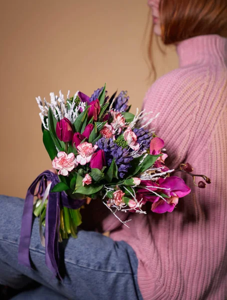 Beautiful woman in rose sweater and jeans holding colored bouquet of tulips, carnations and other flowers. St. Valentine\'s Day, International Women\'s Day or Mother\'s Day concept