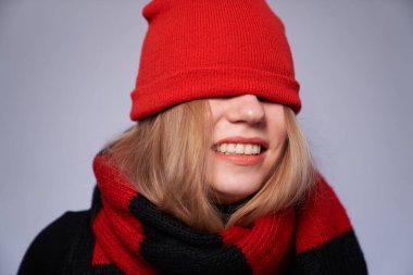 Gri arka planda izole edilmiş kırmızı ve siyah atkısı ve şapkası olan güzel sarışın kız. Kış, sıcak giysi konsepti