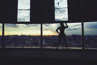 En üst düzey konsept. Gün batımında gökyüzü bulutlarla kaplı binanın tepesinde duran ayakta duran kadın silueti.