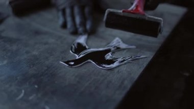 Linocut konsepti. Kuş şeklinde kesilmiş muşamba parçasının üzerinde yuvarlanan boya. Siyah eldivenli bir erkek beyaz pulda siyah mürekkep yuvarlıyor. 4k görüntü
