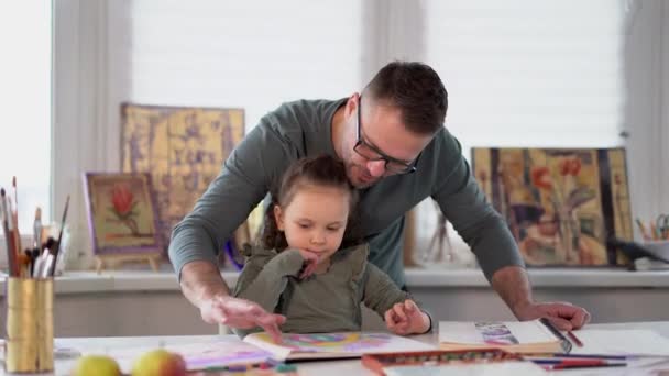 A father helps his little daughter to do her drawing. Happy creative family concept. Caring caucasian dad babysitter drawing with colored pencils teaching child girl. 4k footage