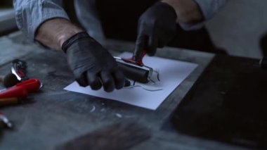 Linocut konsepti. Bir kuş formunda muşamba parçasına baskı yapmak için yuvarlanıyor. Siyah eldivenli bir erkek, kağıt üzerinde iz bırakmak için pul üzerinde yuvarlanıyor. 4k görüntü