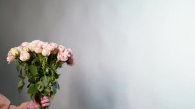 Pembe bluzlu bir kadının elleri gri arka planda saklanmış gül çiçekleri buketiyle tebrik eder. Anneler Günü ya da Uluslararası Kadınlar Günü konseptiyle tebrik ediyorum. 4K görüntü