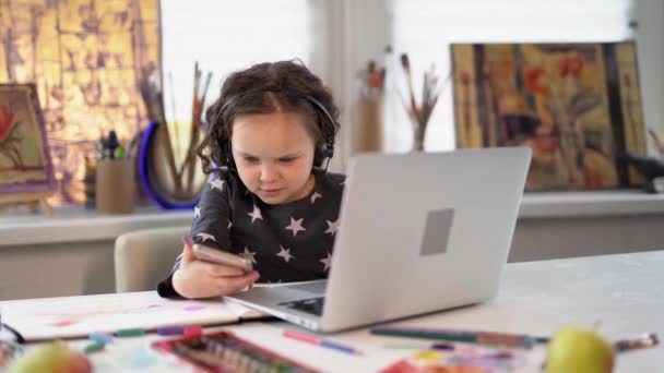 小商人的概念 戴耳机的聪明女孩在网上做作业 或者用智能手机和笔记本电脑做小生意 在检疫期间 戴耳机的孩子在上课 4K镜头 — 图库视频影像