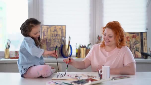 어머니와 집에서 페인트 물감으로 그림을 그리고 있습니다 소녀는 앉아서 딸에게 — 비디오
