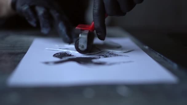 Muž v černých rukavicích dělá linokut pták razítko na papíře — Stock video