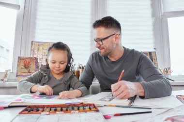 Mutlu aile hobisi: baba ve kızı birlikte çiziyorlar.