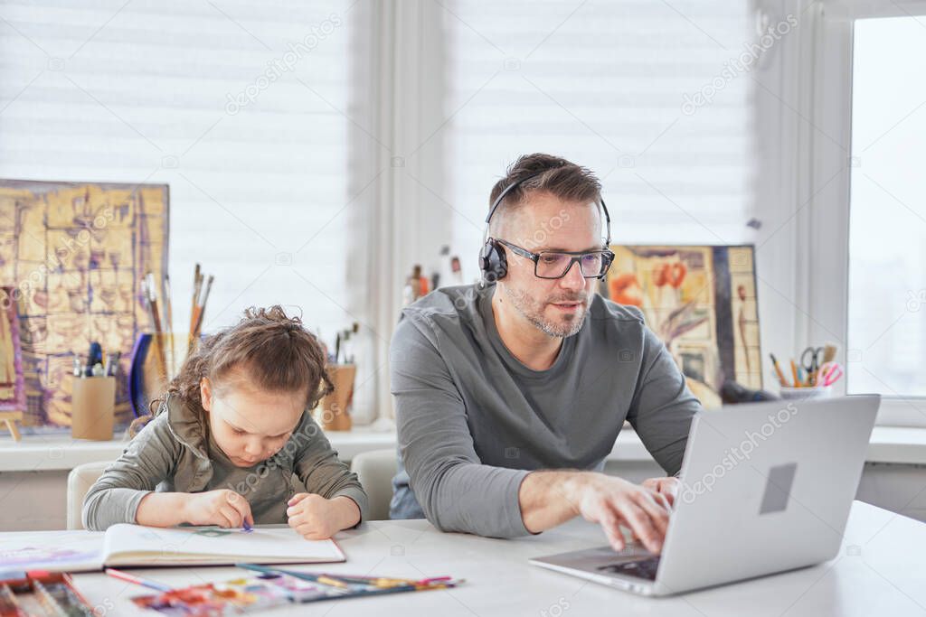 Quarantine: small girl drawing and dad working on laptop