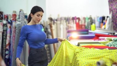 Kadın müşteri tekstil dükkanında sarı kumaş atıyor.