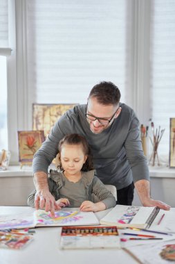 Mutlu bir baba, küçük kızının kalemle çizmesine yardım ediyor.