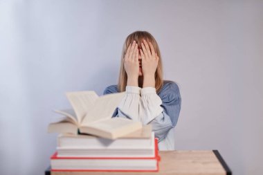 Öğrenci kız kitaplarla oturuyor ve elleriyle gözlerini kapatıyor. 