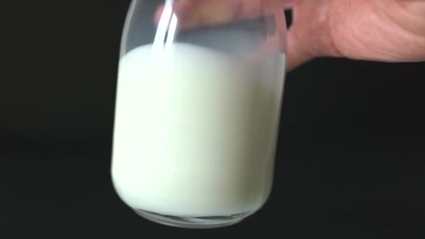 Hand schudden van een glas verse melk op een zwarte achtergrond — Stockvideo