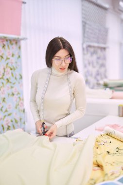 Kadın terzi, profesyonel makasla kumaş kesiyor.