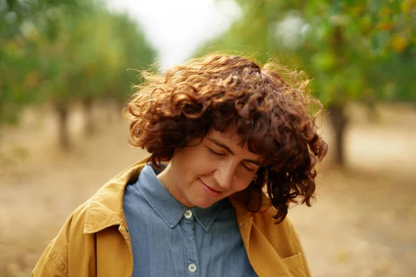 Mujer rizada en chaqueta naranja relajándose en el parque de otoño — Foto de Stock