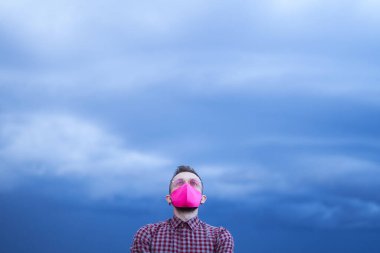 Pembe maskeli, yağmurlu mavi gökyüzü olan adam yukarı bakıyor.