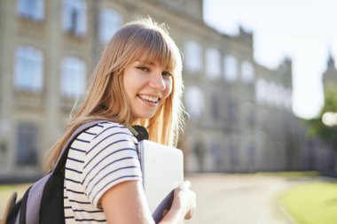 Kampüste dizüstü bilgisayarı olan neşeli gülümseyen üniversite öğrencisi.